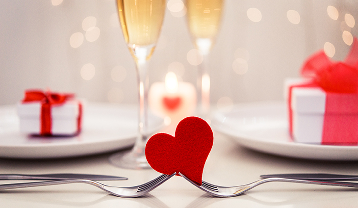Two forks holding a felt heart in front of champagne glasses