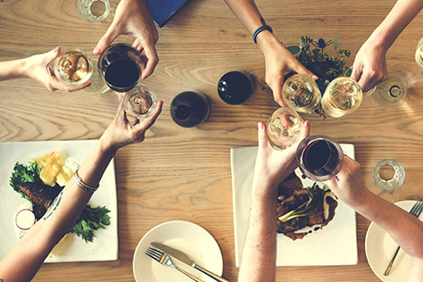 clinking wine glasses over a table with food.